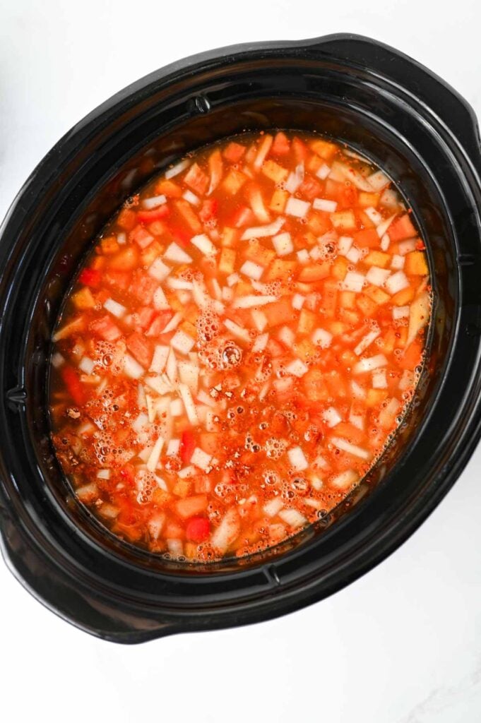 chicken broth and enchilada sauce aded to slow cooker with diced red bell peppers and onions