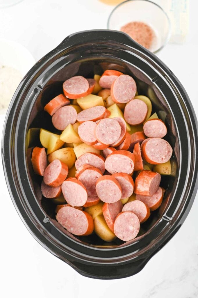 sausage slices on top of chopped potatoes ina slow cooker