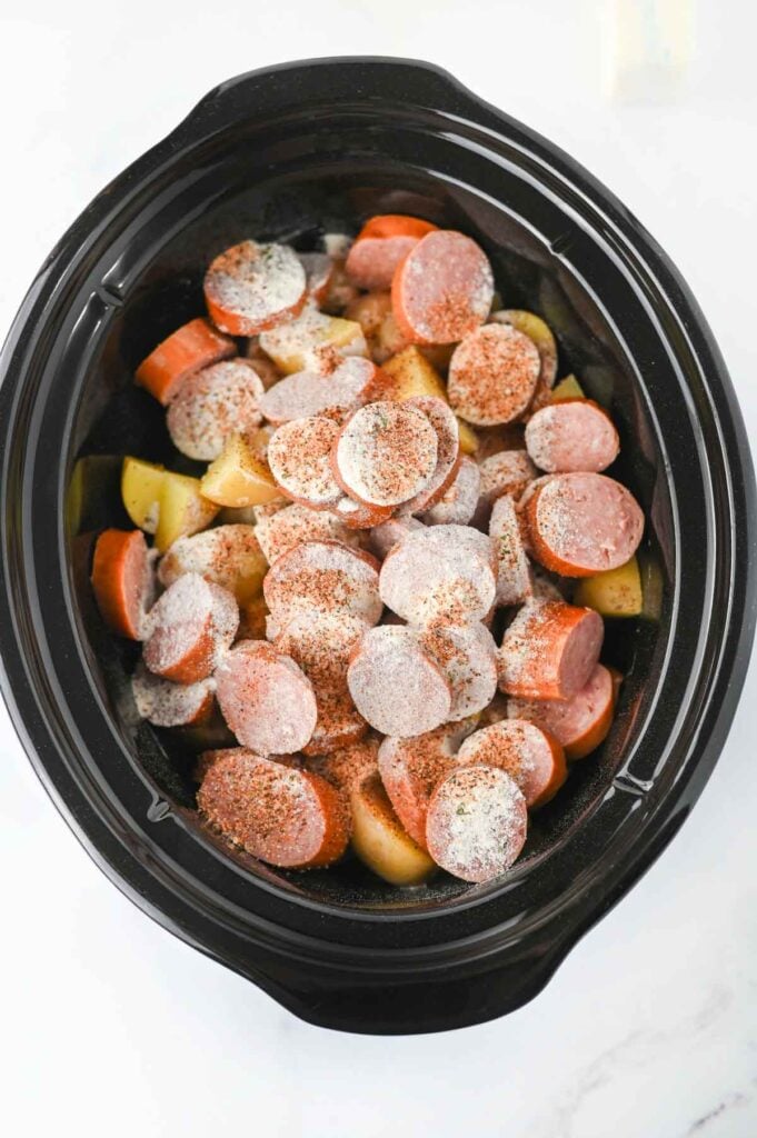 ranch seasoning and cajun seasoning on top of sausage slices and chopped potatoes in a slow cooker