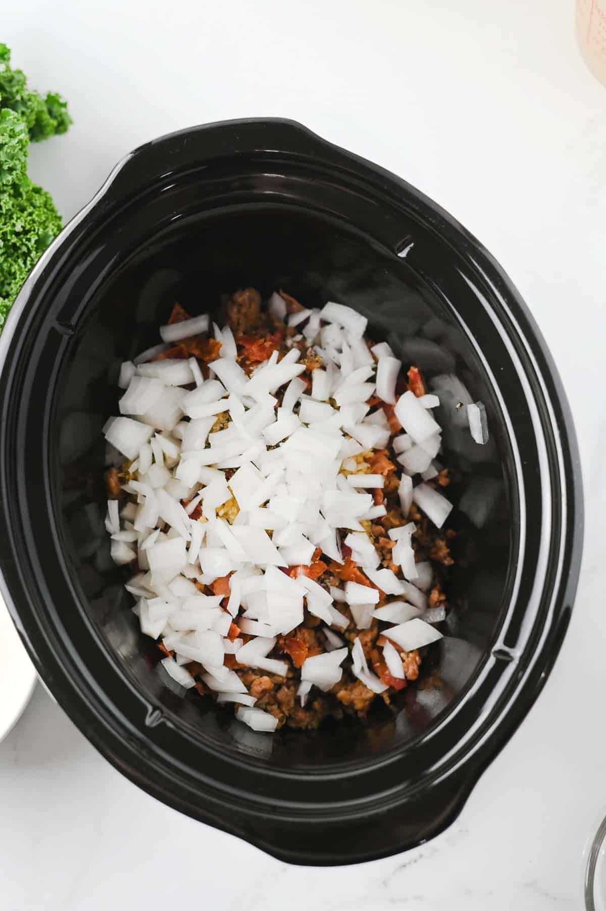 diced onions on top of cooked sausage and bacon in a slow cooker