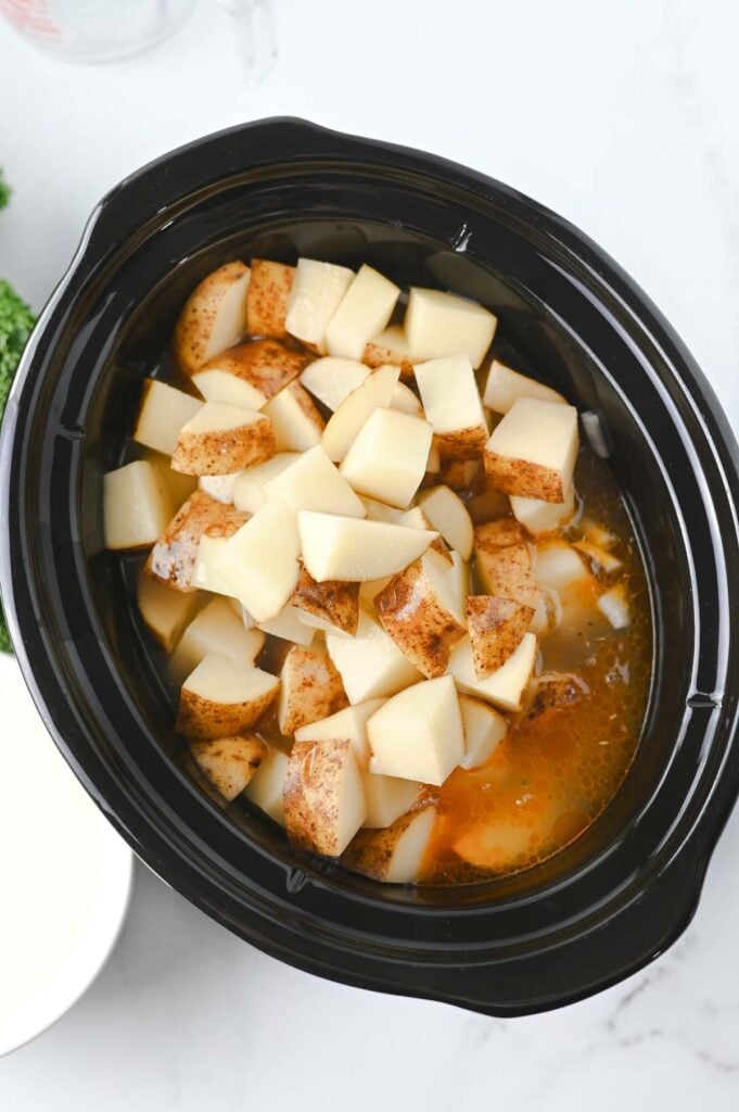 potato chunks and chicken broth added to slow cooker with sausage meat and bacon