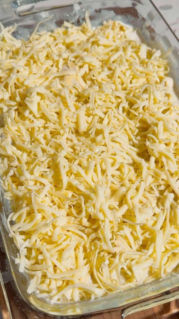 shredded mozzarella on top of tortellini alfredo in a baking dish
