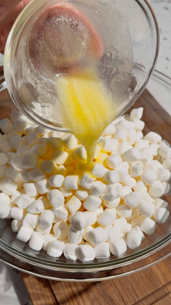 melted butter being poured over mini marshmallows in a glass bowl