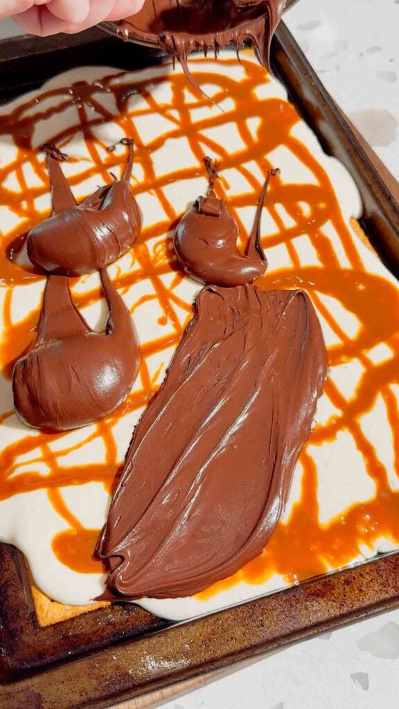 melted chocolate spoon over marshmallow and caramel layer of s'mores bars
