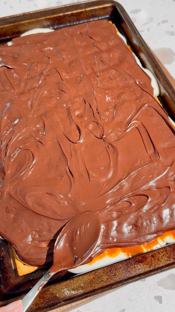 melted chocolate spread over marshmallow layer of s'mores bars
