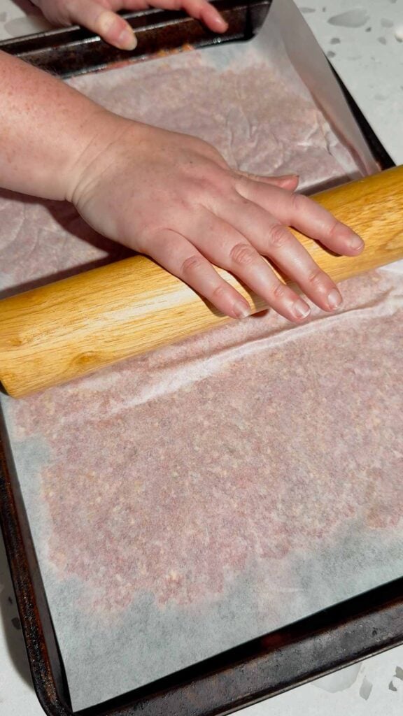rolling pin on top of meat mixture covered with parchment paper