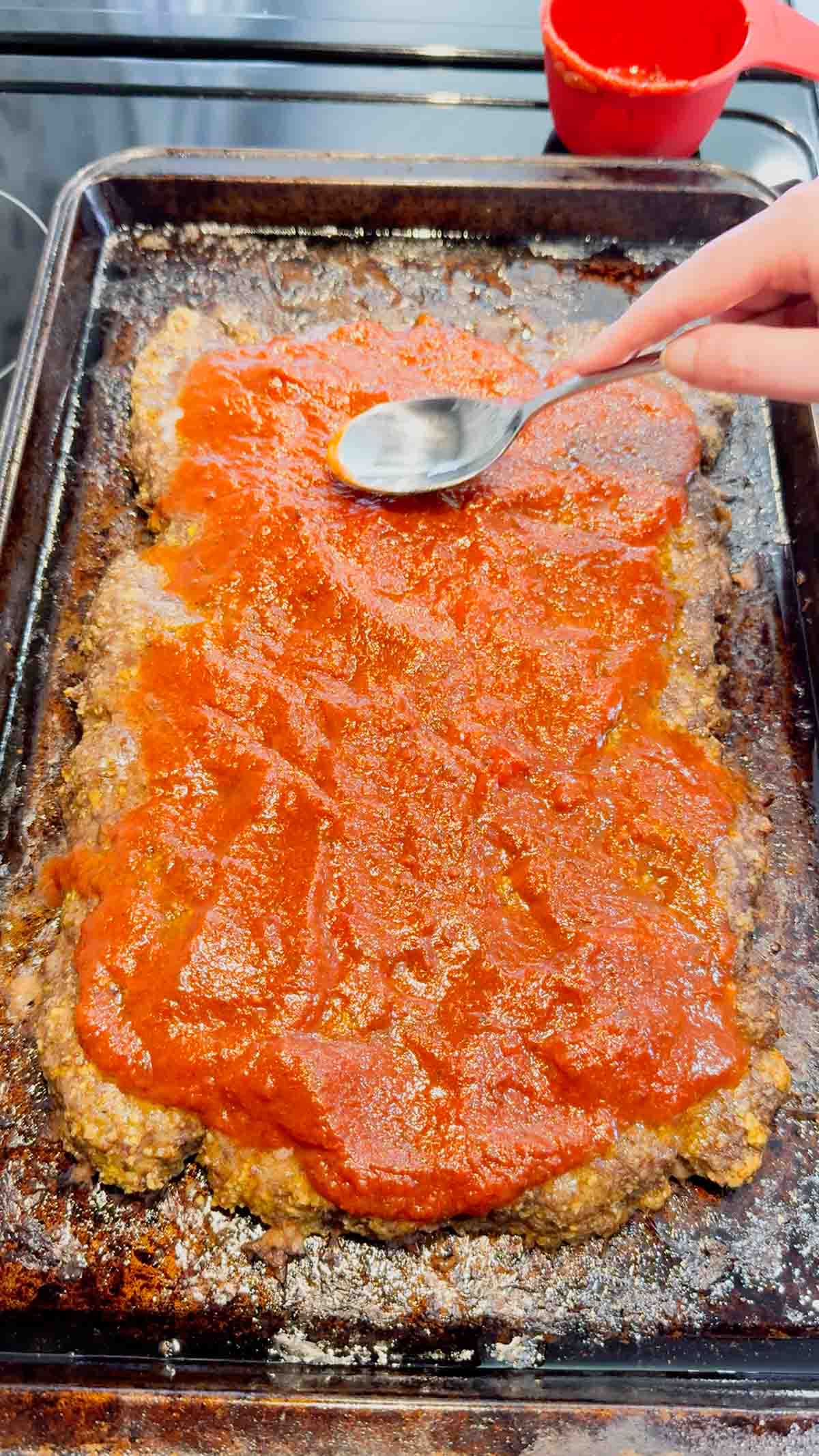 pizza sauce spread on top of meatloaf on a baking sheet