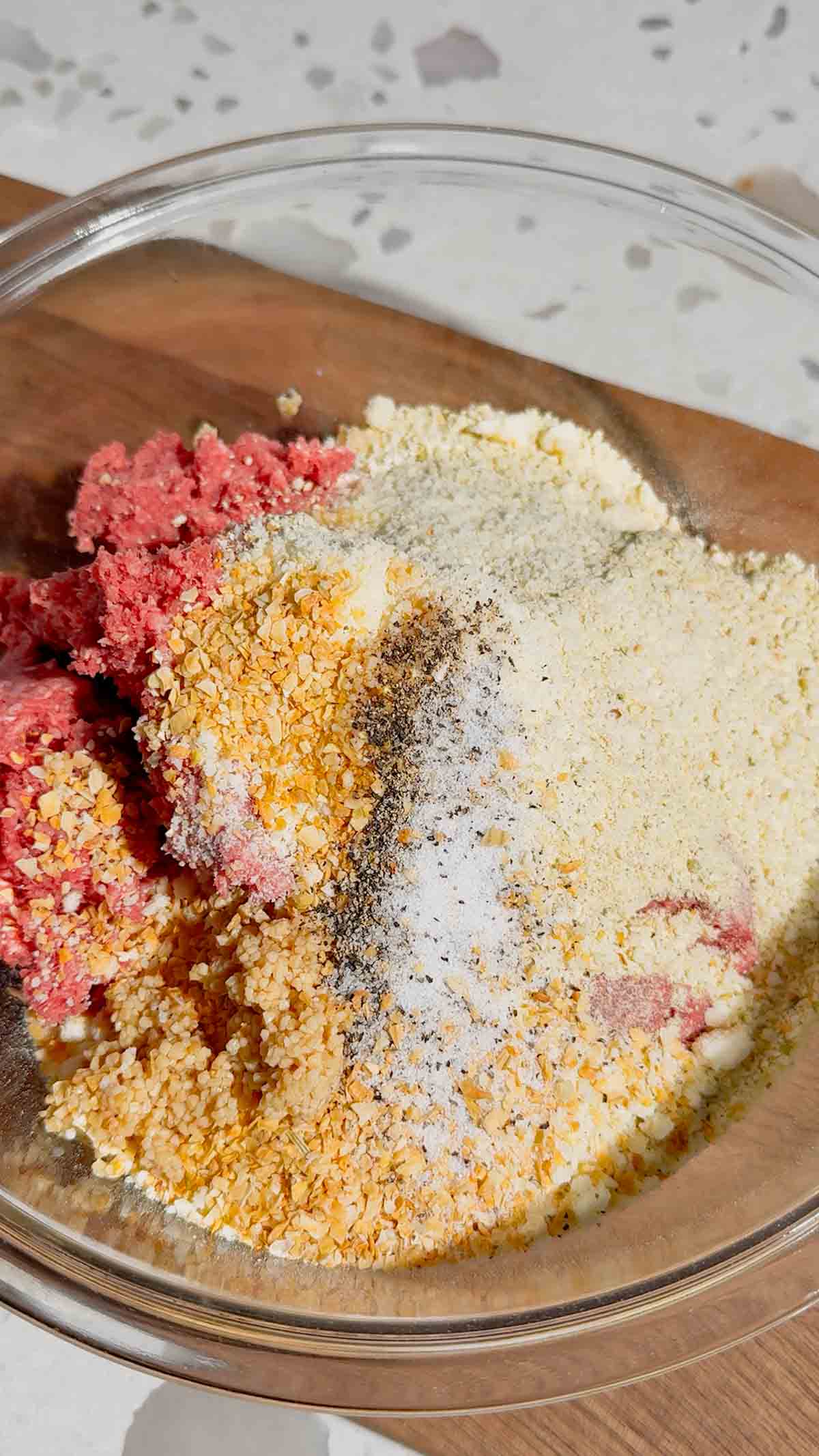 salt, pepper, minced onion, chopped garlic, parmesan cheese, and bread crumbs on top of raw ground beef in a mixing bowl