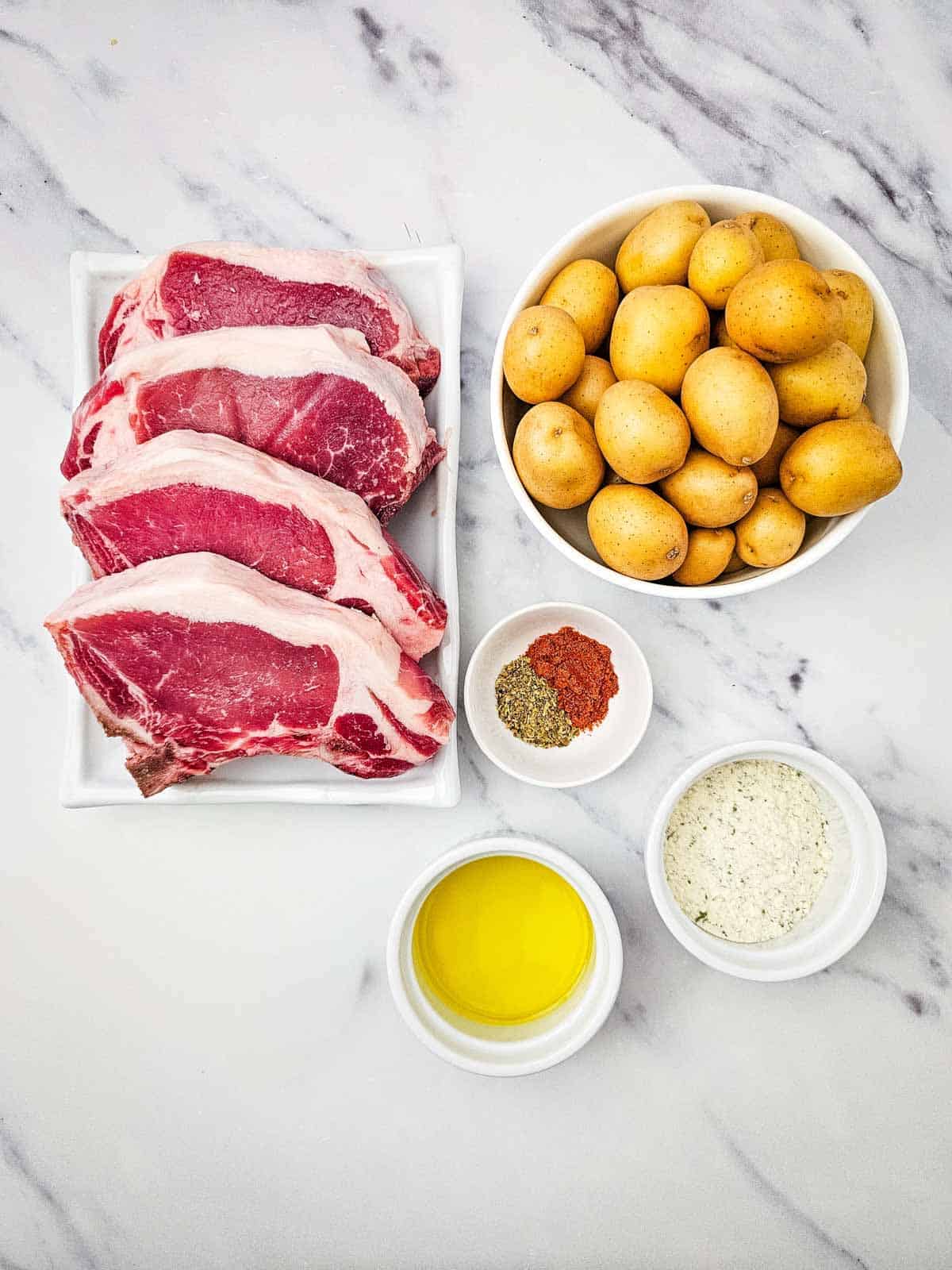raw pork chops, small potatoes and seasonins on the ktichen counter