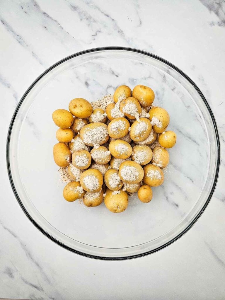 ranch seasoning blend poured over baby potatoes in glass mixing bowl