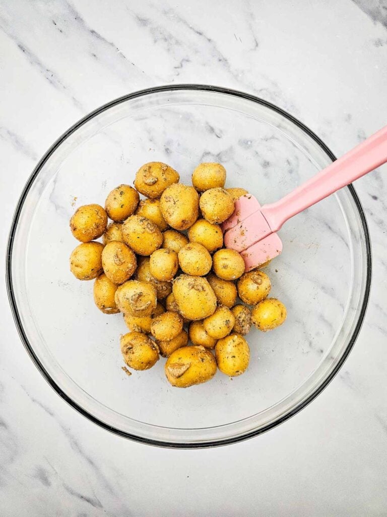 baby potatoes tossed with olive oil and ranch seasoning mixture in a glass mixing bowl