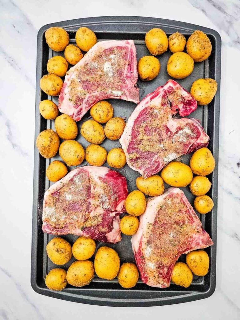 seasoned pork chops and baby potatoes on a sheet pan