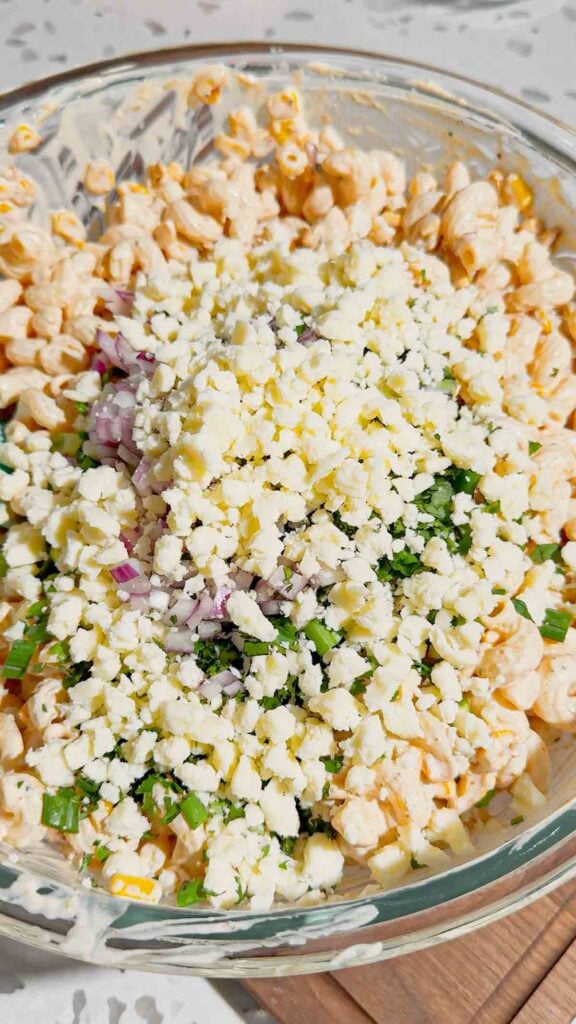 crumbled cojita added to bowl with street corn pasta salad ingredients