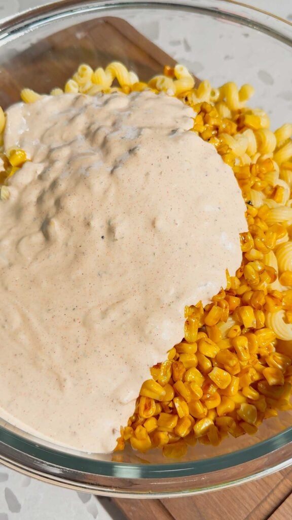 creamy dressing poured over cooked pasta and corn in a mixing bowl