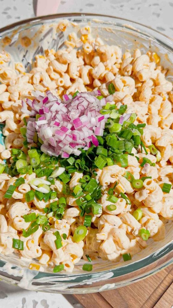 diced red onion and chopped green onions added to pasta salad mixture in a mixing bowl