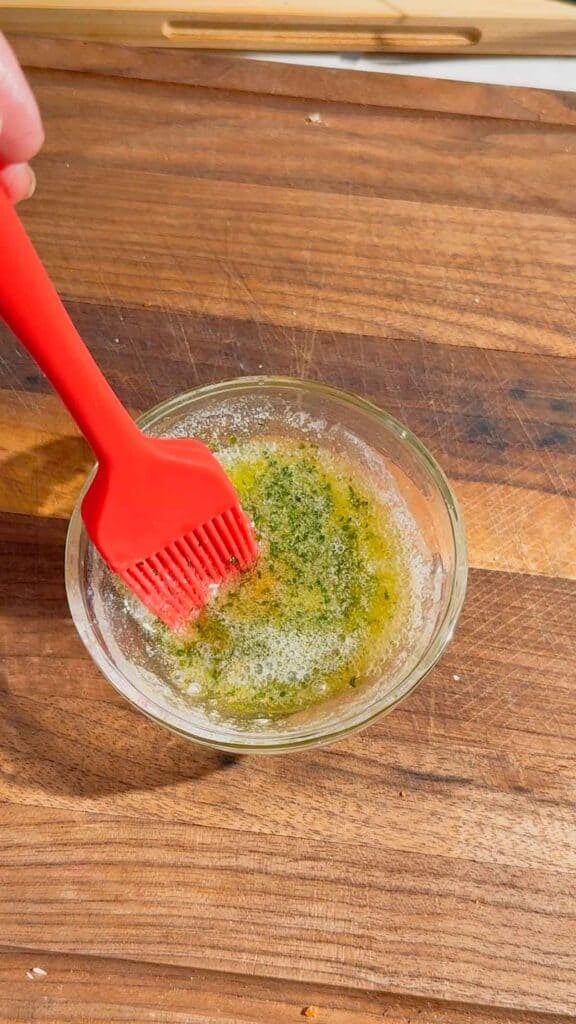 melted butter, garlic powder and parsley being stirred together in a small bowl