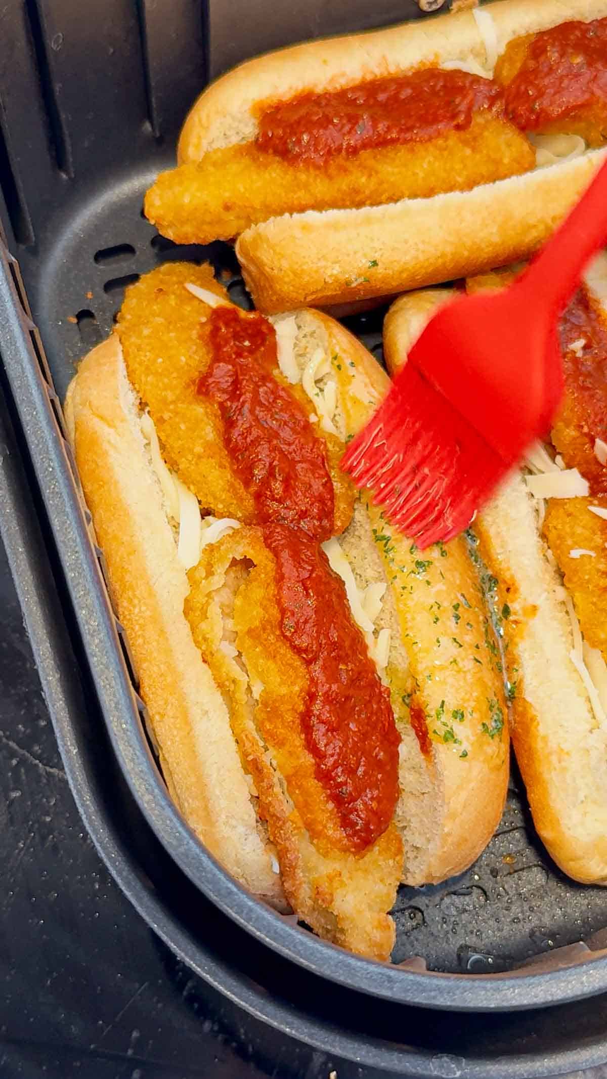 brushing melted garlic butter on crispy chicken subs in an air fryer basket