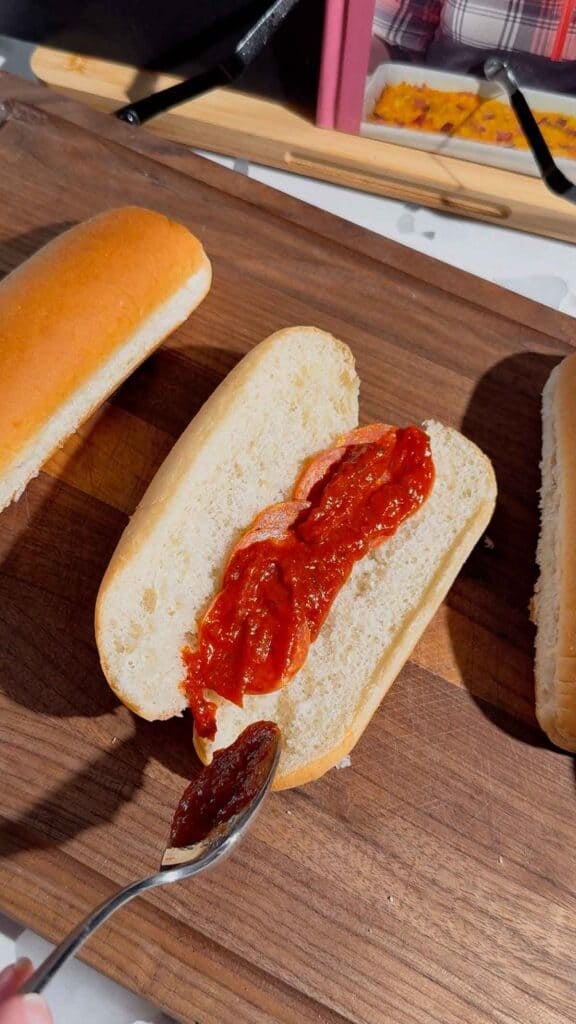 pizza sauce on top of pepperoni slices in a hot dog bun