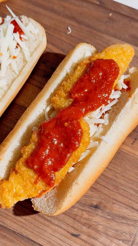 pizza sauce on top of chicken fingers and shredded cheese in a hot dog bun