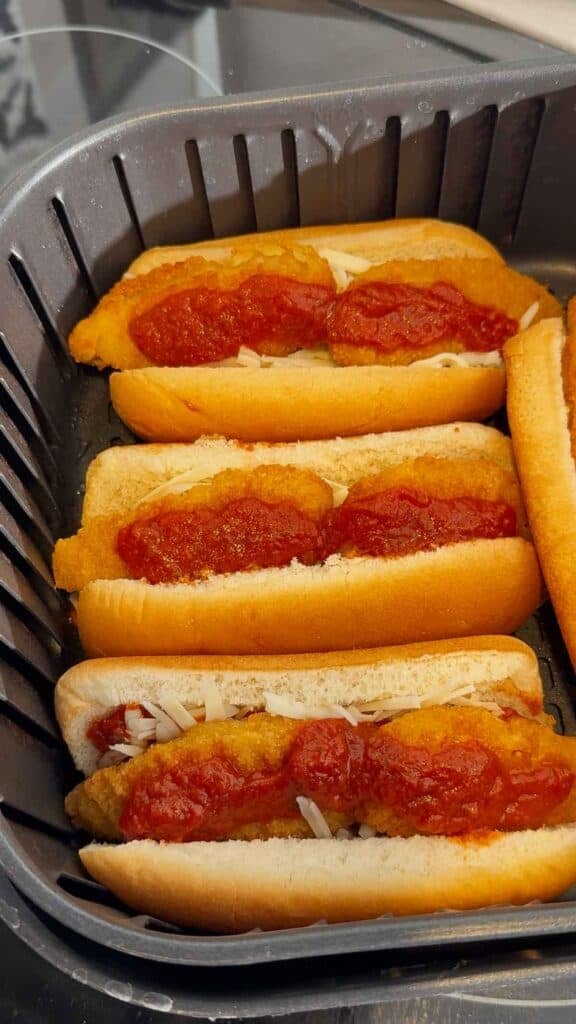 pizza sauce on top of chicken fingers in buns in an air fryer basket