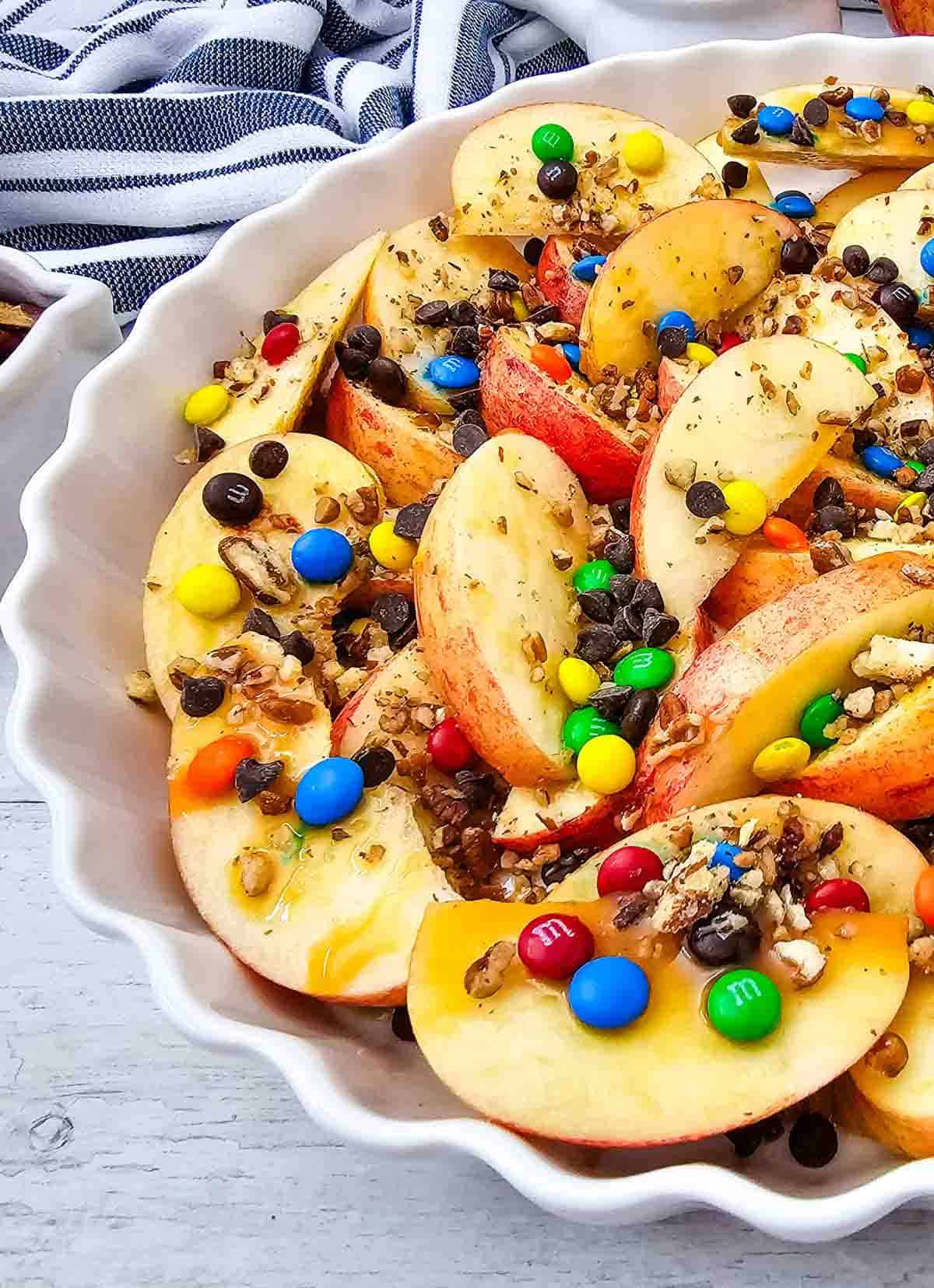 Looking for a fun, easy, and crowd-pleasing snack? These Apple Nachos are the ultimate no-bake dessert recipe made with crisp fresh apples, rich caramel sauce, mini chocolate chips, colorful mini M&Ms, and crunchy pecans. Ready in just 10 minutes, they're perfect for easy fall desserts, healthy-ish snacks for kids, after school snacks, party food ideas, apple dessert recipes, sweet snack recipes, Halloween treats, Thanksgiving snacks, and quick family desserts. Whether you're searching for caramel apple recipes, apple slices with toppings, no bake apple desserts, or a simple fruit dessert everyone will love, these loaded Apple Nachos are a delicious way to enjoy fresh apples with a fun candy twist. Save this easy recipe for your next snack craving or celebration!
