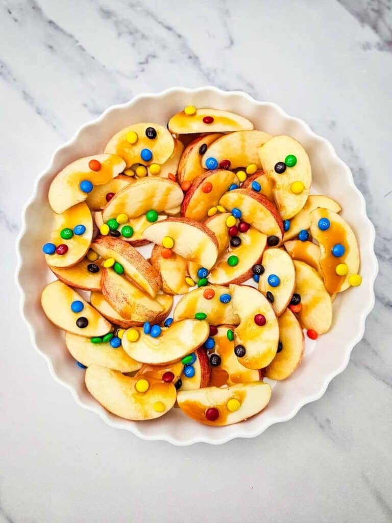 caramel sauce and m and m s candies on top of apple slices in a serving dish