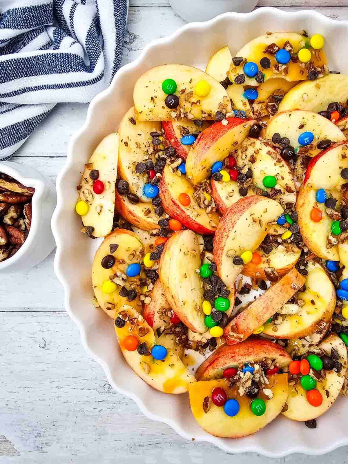 Looking for a fun, easy, and crowd-pleasing snack? These Apple Nachos are the ultimate no-bake dessert recipe made with crisp fresh apples, rich caramel sauce, mini chocolate chips, colorful mini M&Ms, and crunchy pecans. Ready in just 10 minutes, they're perfect for easy fall desserts, healthy-ish snacks for kids, after school snacks, party food ideas, apple dessert recipes, sweet snack recipes, Halloween treats, Thanksgiving snacks, and quick family desserts. Whether you're searching for caramel apple recipes, apple slices with toppings, no bake apple desserts, or a simple fruit dessert everyone will love, these loaded Apple Nachos are a delicious way to enjoy fresh apples with a fun candy twist. Save this easy recipe for your next snack craving or celebration!
