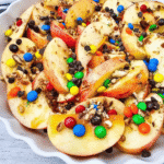 Looking for a fun, easy, and crowd-pleasing snack? These Apple Nachos are the ultimate no-bake dessert recipe made with crisp fresh apples, rich caramel sauce, mini chocolate chips, colorful mini M&Ms, and crunchy pecans. Ready in just 10 minutes, they're perfect for easy fall desserts, healthy-ish snacks for kids, after school snacks, party food ideas, apple dessert recipes, sweet snack recipes, Halloween treats, Thanksgiving snacks, and quick family desserts. Whether you're searching for caramel apple recipes, apple slices with toppings, no bake apple desserts, or a simple fruit dessert everyone will love, these loaded Apple Nachos are a delicious way to enjoy fresh apples with a fun candy twist. Save this easy recipe for your next snack craving or celebration!