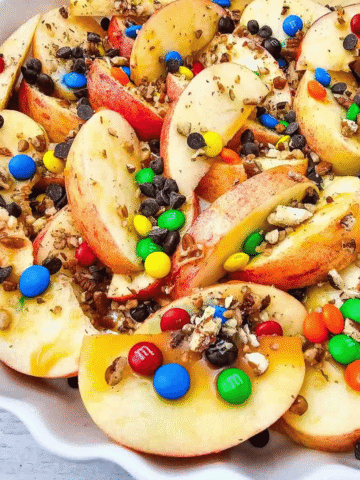 Looking for a fun, easy, and crowd-pleasing snack? These Apple Nachos are the ultimate no-bake dessert recipe made with crisp fresh apples, rich caramel sauce, mini chocolate chips, colorful mini M&Ms, and crunchy pecans. Ready in just 10 minutes, they're perfect for easy fall desserts, healthy-ish snacks for kids, after school snacks, party food ideas, apple dessert recipes, sweet snack recipes, Halloween treats, Thanksgiving snacks, and quick family desserts. Whether you're searching for caramel apple recipes, apple slices with toppings, no bake apple desserts, or a simple fruit dessert everyone will love, these loaded Apple Nachos are a delicious way to enjoy fresh apples with a fun candy twist. Save this easy recipe for your next snack craving or celebration!