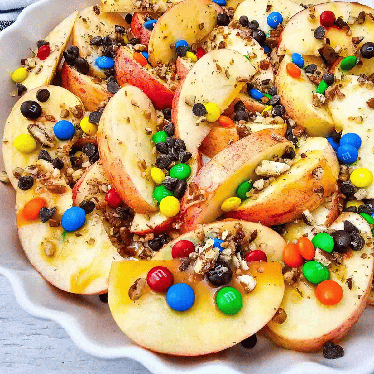 Looking for a fun, easy, and crowd-pleasing snack? These Apple Nachos are the ultimate no-bake dessert recipe made with crisp fresh apples, rich caramel sauce, mini chocolate chips, colorful mini M&Ms, and crunchy pecans. Ready in just 10 minutes, they're perfect for easy fall desserts, healthy-ish snacks for kids, after school snacks, party food ideas, apple dessert recipes, sweet snack recipes, Halloween treats, Thanksgiving snacks, and quick family desserts. Whether you're searching for caramel apple recipes, apple slices with toppings, no bake apple desserts, or a simple fruit dessert everyone will love, these loaded Apple Nachos are a delicious way to enjoy fresh apples with a fun candy twist. Save this easy recipe for your next snack craving or celebration!