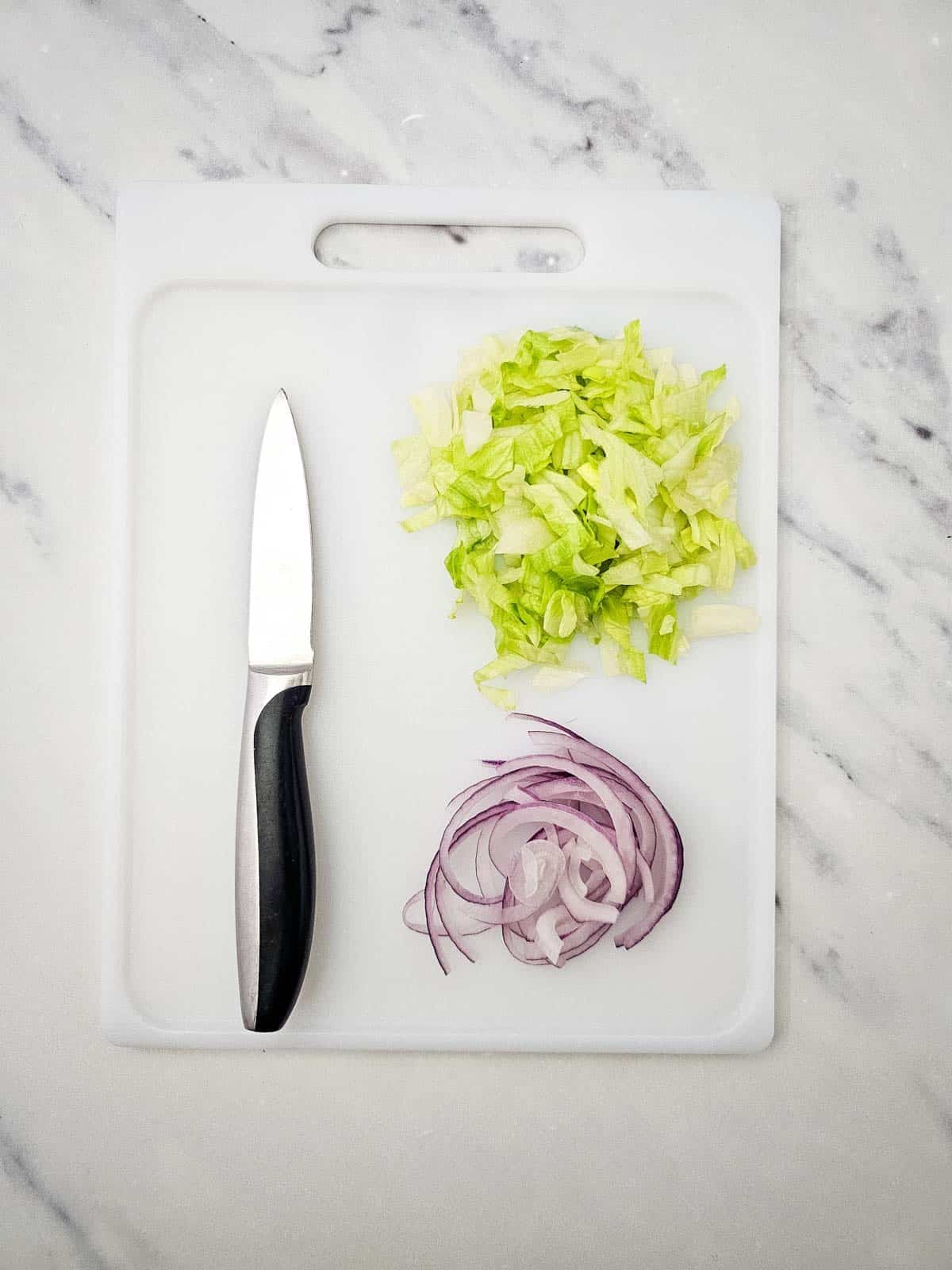chopped lettuce and red onion slices on a cutting board