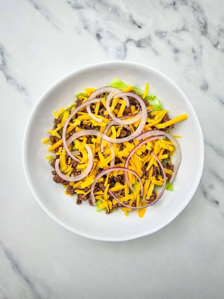 red onions, shredded cheddar and ground beef on top of lettuce in a bowl