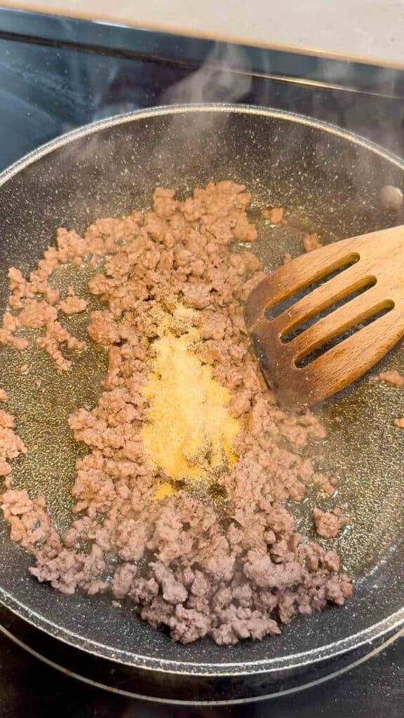 seasonings on top of cooked ground beef in a skillet