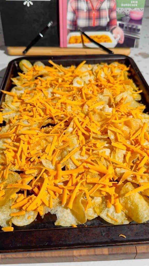 shredded cheddar cheese on top of kettle chips on a baking sheet