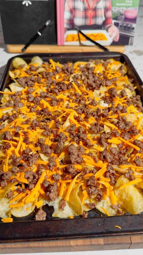 cooked ground beef and shredded cheddar cheese on top of kettle chips on a baking sheet