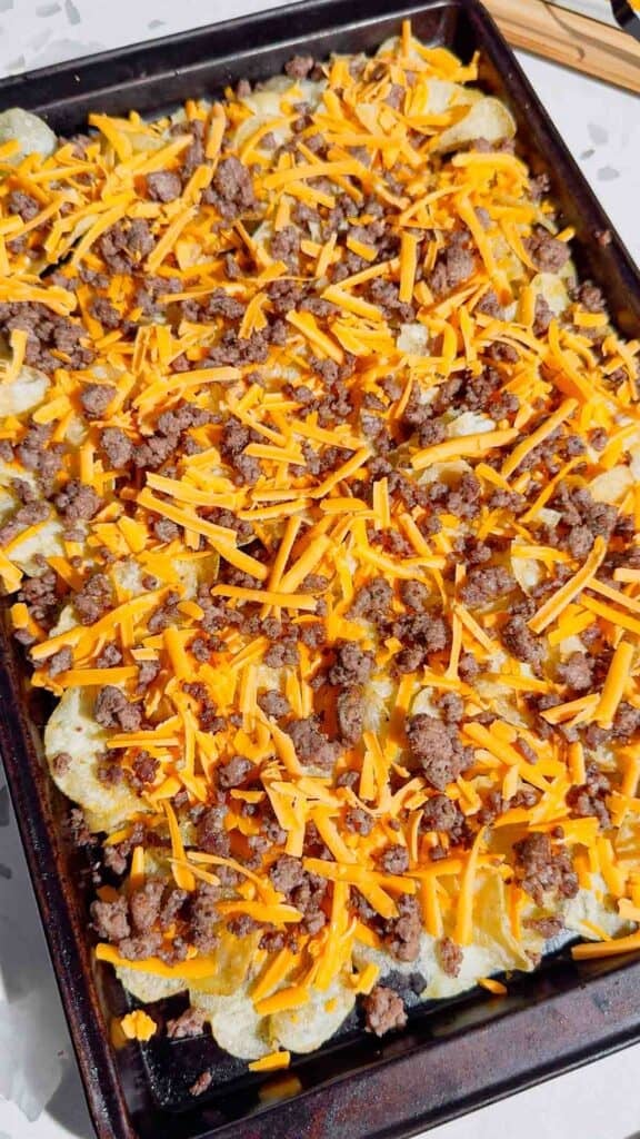 shredded cheddar cheese and cooked ground beef on top of kettle chips on a baking sheet