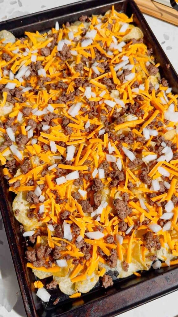 diced onions, cheddar cheese and ground beef on top of kettle chips on a baking sheet