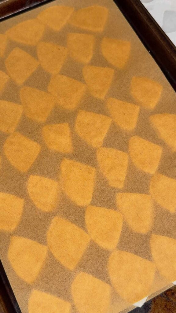 biscuit pieces between to sheets of parchment paper on a a baking sheet