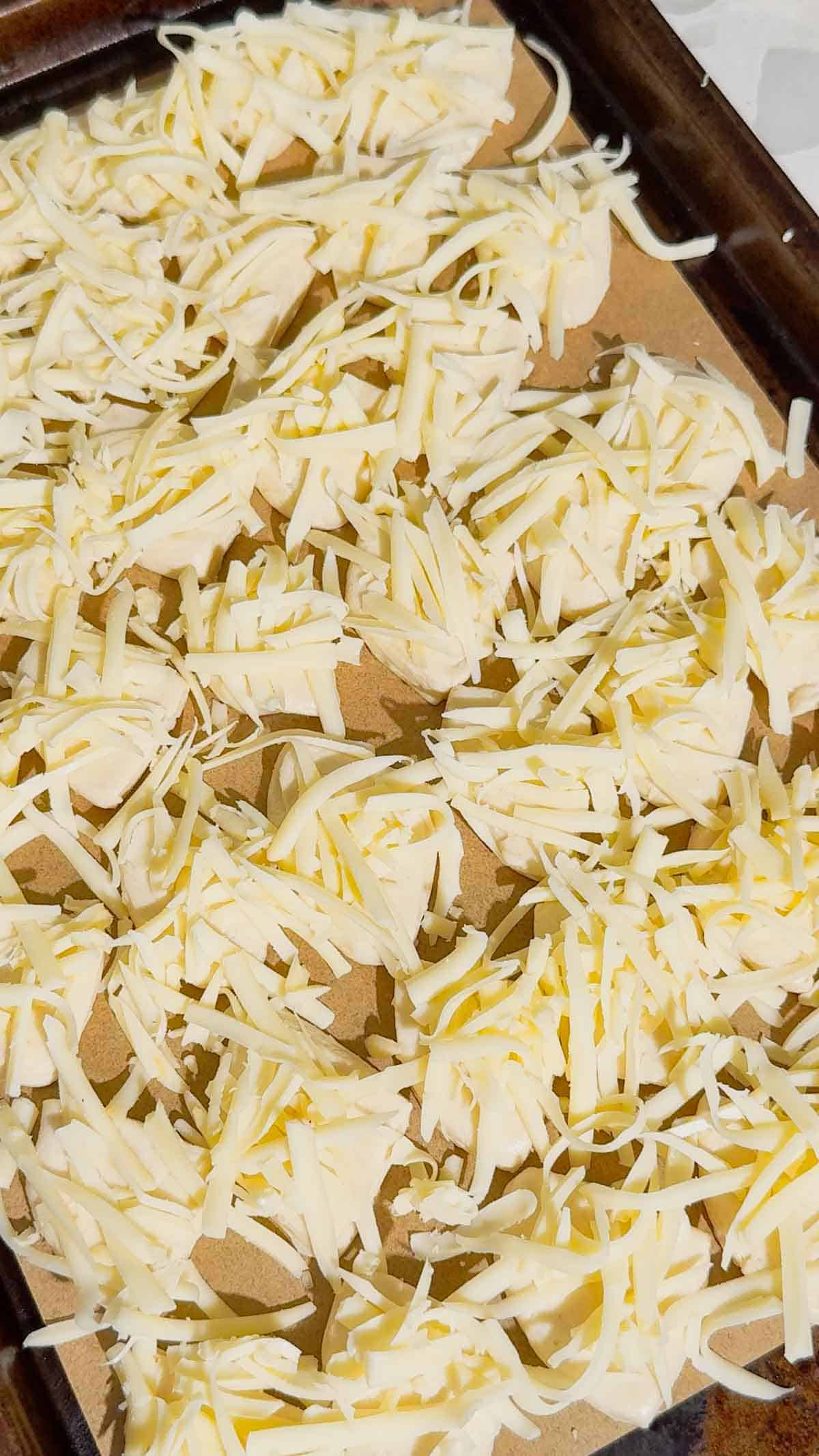 shredded mozzarella cheese on top of biscuit pieces on a parchment lined baking sheet