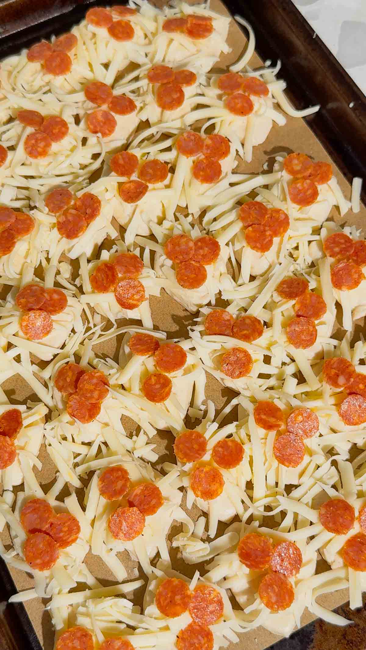 mini pepperonis and shredded mozzarella cheese on top of biscuit pieces on a parchment lined baking sheet