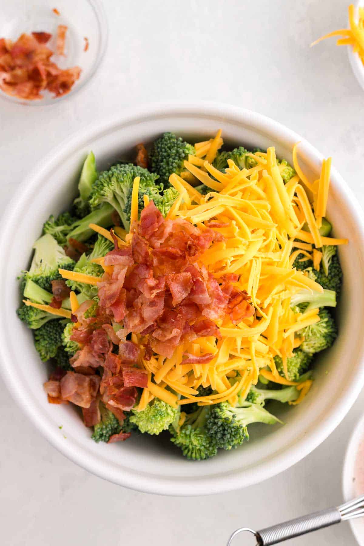 shredded cheddar and chopped bacon on top of broccoli florets in a bowl