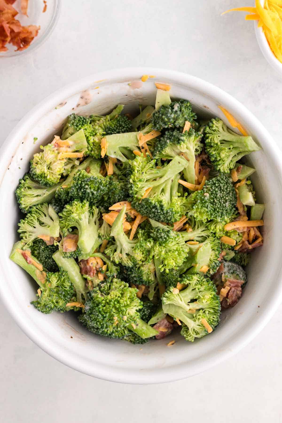 broccoli salad being tossed with dressing in a bowl