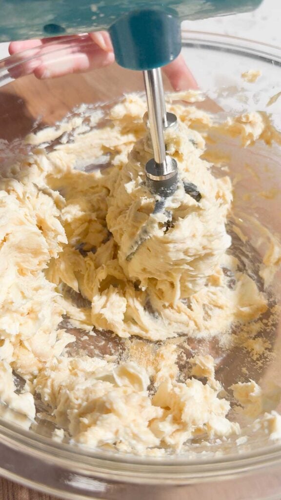 electric mixer creaming together butter, cream cheese and sugar in a mixing bowl