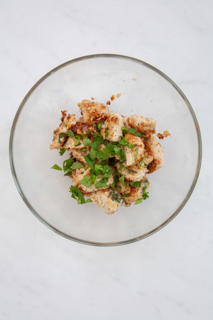 chopped cilantro on top of cooked chicken breast chunks in a glass bowl
