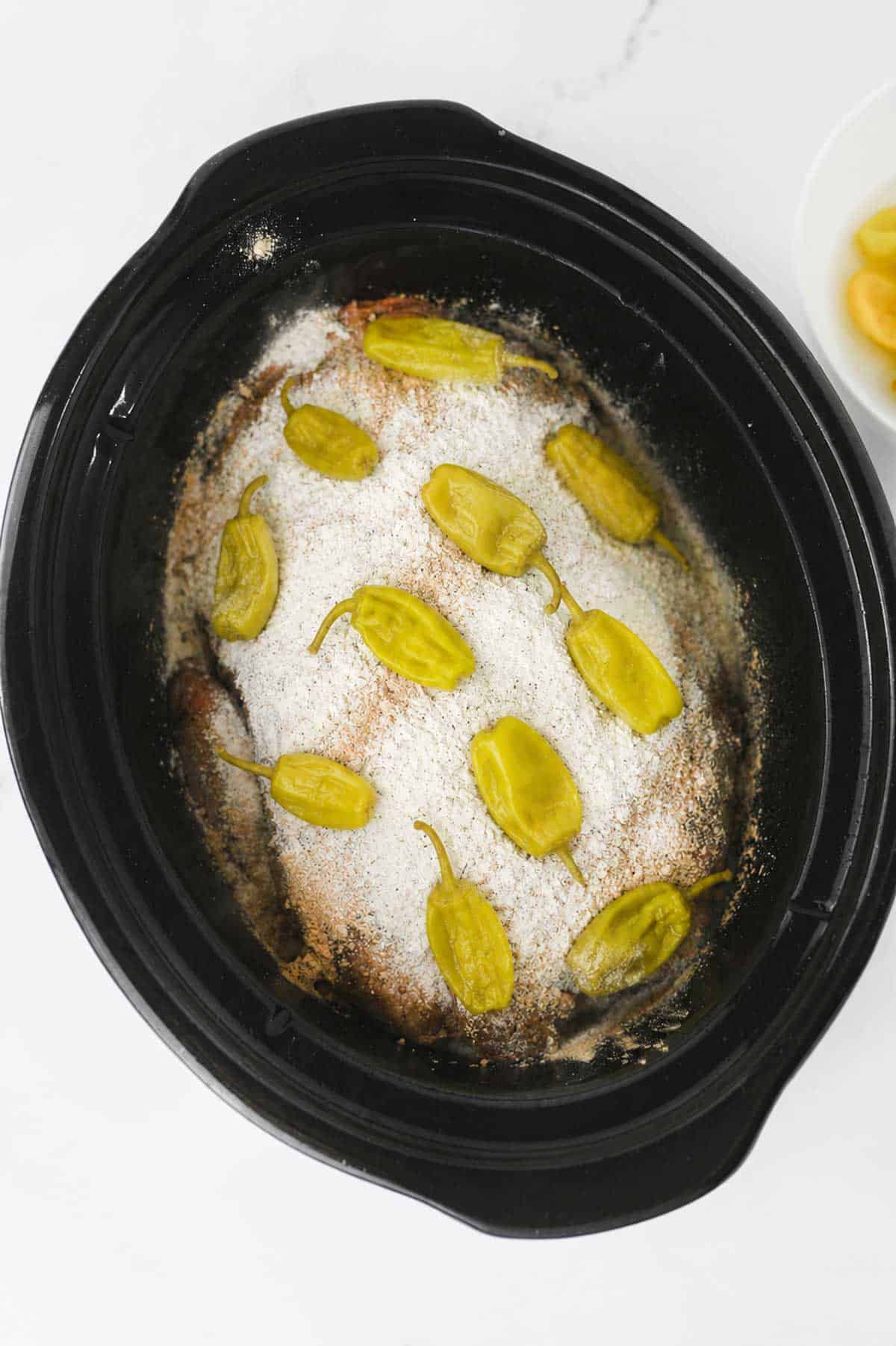 pepperoncini peppers on top of ranch dressing mix and pot roast in a slow cooker
