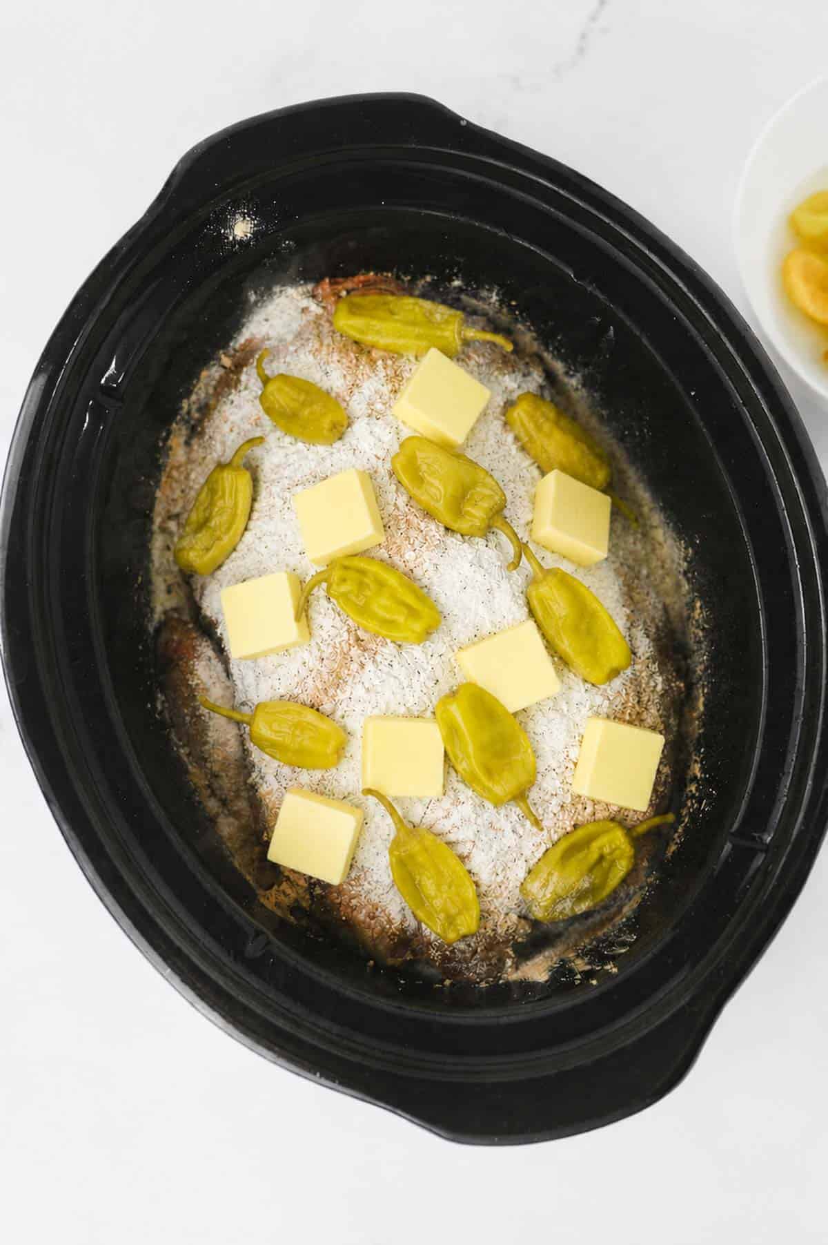 butter and pepperoncini peppers on top of ranch dressing mix and pot roast in a crock pot