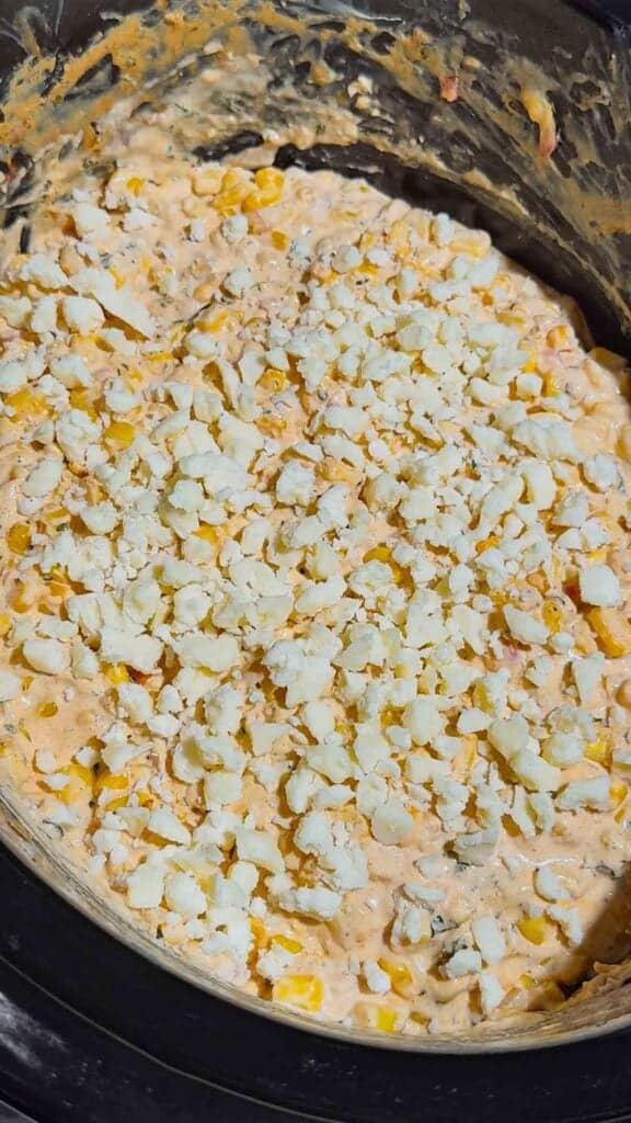crumbled cotija cheese on top of street corn dip in a slow cooker