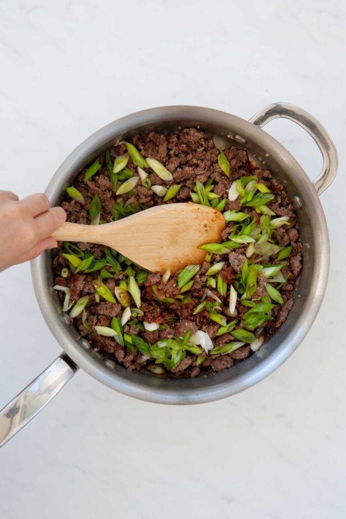stirring green onions into korean ground beef in a skillet