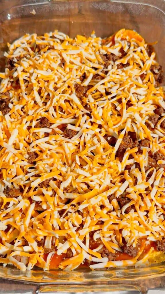 shredded cheddar on top of ground beef and tortilla chips in a baking dish