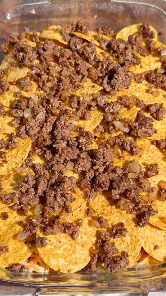 ground beef on top of tortilla chip layer in a baking dish